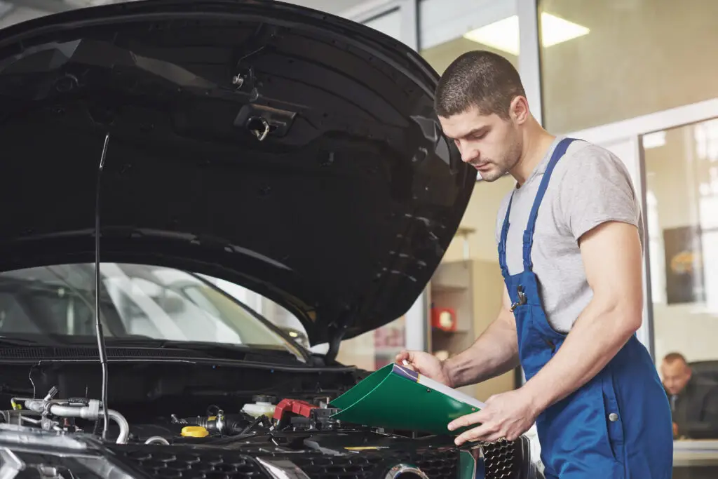 car service, repair, maintenance and people concept - auto mechanic man or smith with clipboard at workshop.